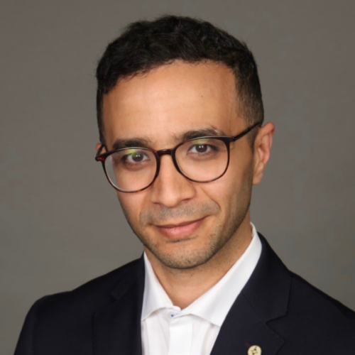 Photo of George Ibrahim wearing glasses, a white shirt, and a dark blazer