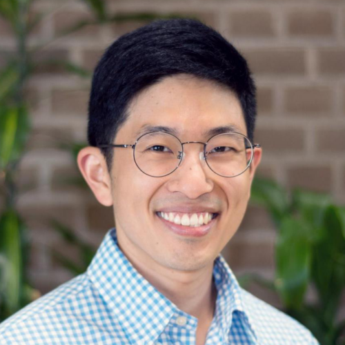 Photo of Sanghyun (Kris) Kim against a brick wall, wearing glasses and blue checked shirt