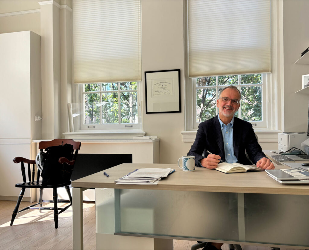 A photo of Provost Trevor Young sitting at his desk wearing a navy blue jacket and light blue shirt