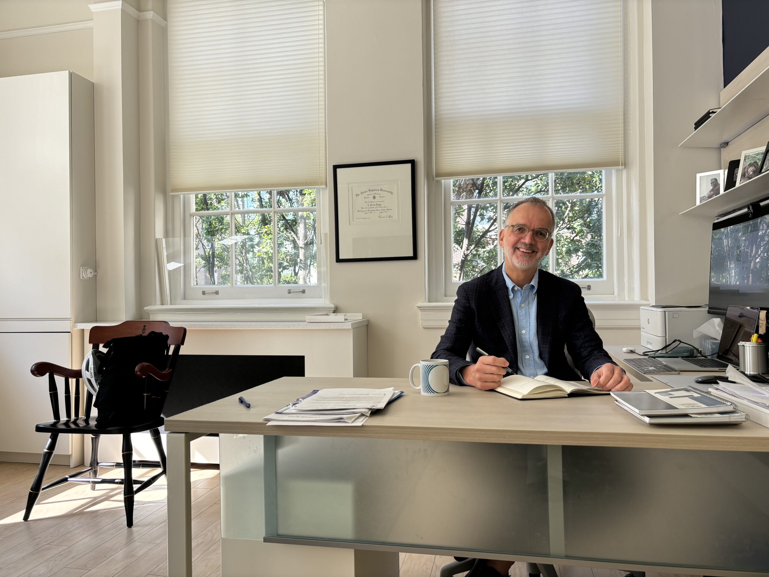 A photo of Provost Trevor Young sitting at his desk wearing a navy blue jacket and light blue shirt